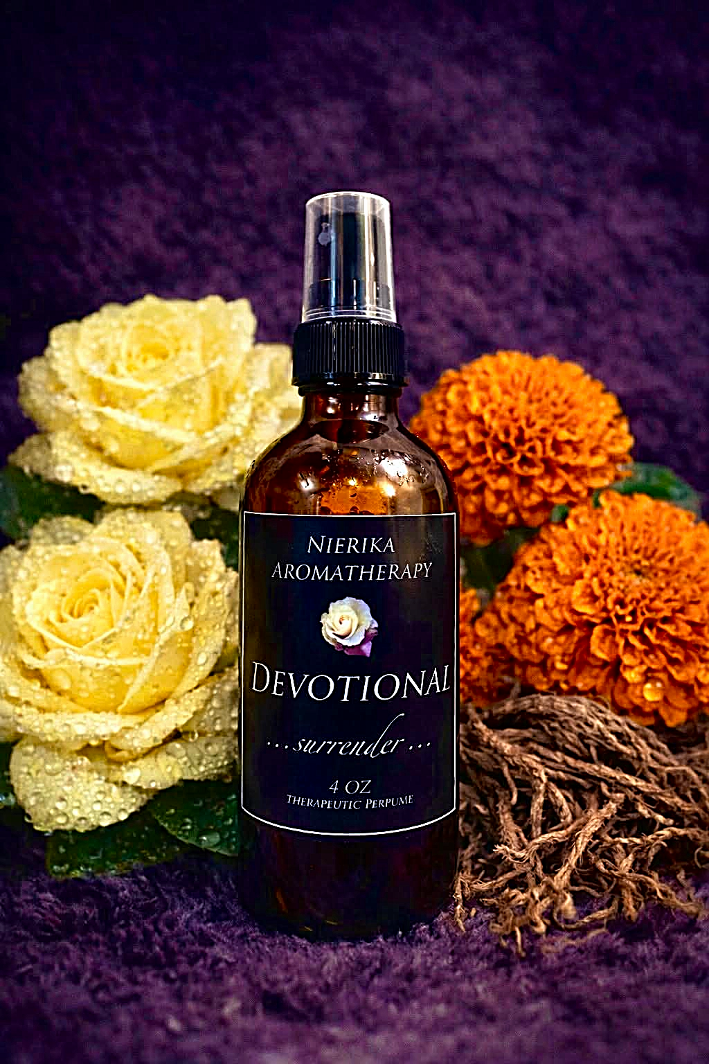 Devotional therapeutic perfume spray by Nierika Aromatherapy, surrender blend with marigold flowers and roses – 4 oz bottle on purple fabric