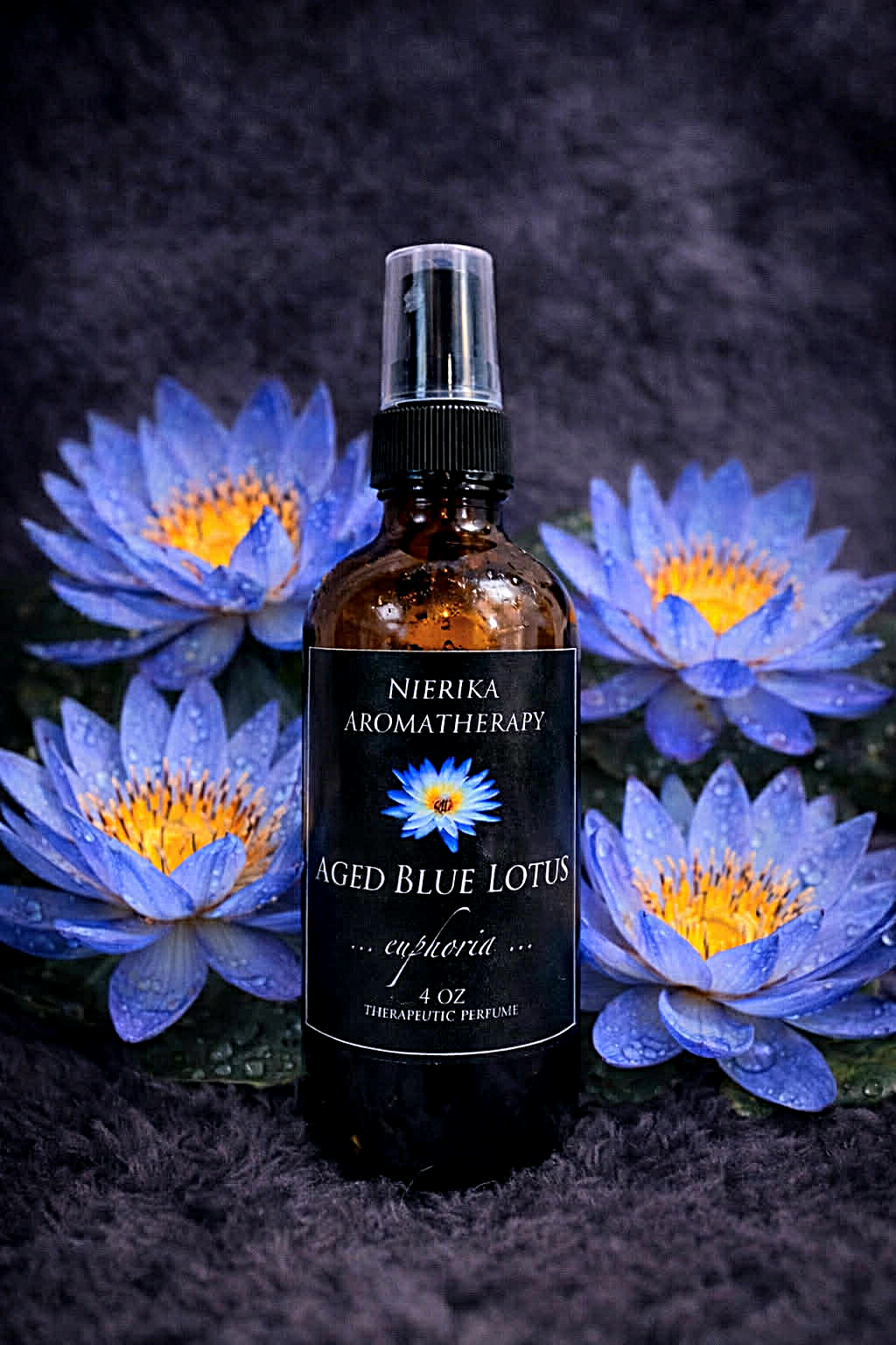 Aged Blue Lotus therapeutic perfume spray by Nierika Aromatherapy, euphoria blend, bottle among blue lotus flowers on dark fabric – 4 oz